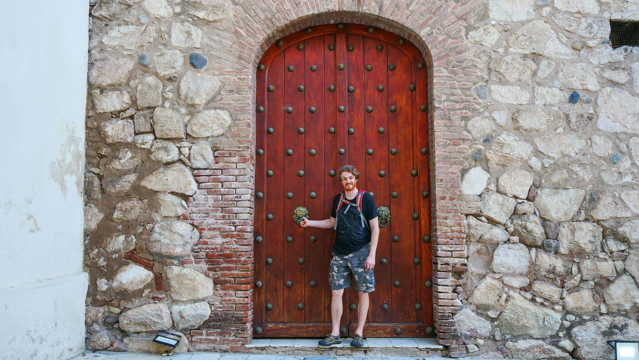 Nomadic Samuel wishing he could leverage his height standing beside an impressively large door in Cordoba City, Argentina