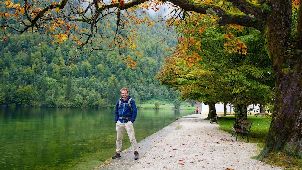 Samuel Jeffery, global investor and creator of Picture Perfect Portfolios (also known as globetrotter Nomadic Samuel), pausing on a lakeside hiking path surrounded by autumn colors in the German Alps.